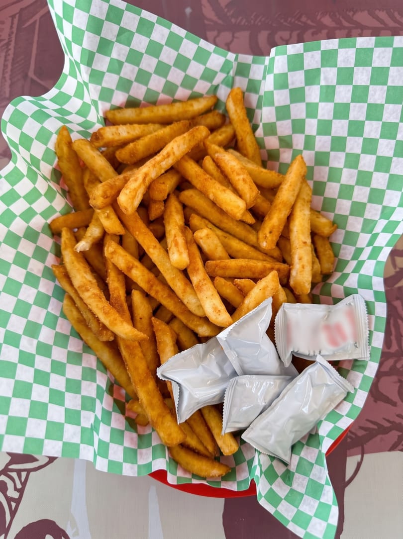 A basket of seasoned french fries in green and white checkered paper with ketchup packets.