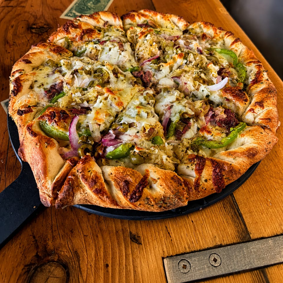 A freshly baked pizza with a braided crust, topped with cheese, green peppers, onions, and sauerkraut.