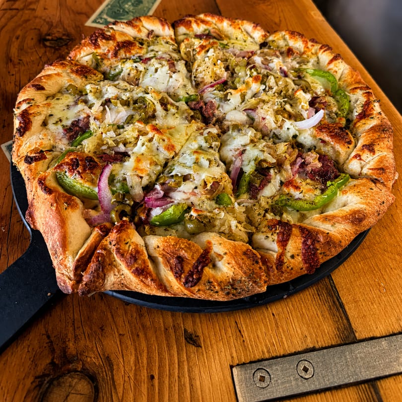 A freshly baked pizza with a braided crust, topped with cheese, green peppers, onions, and sauerkraut.