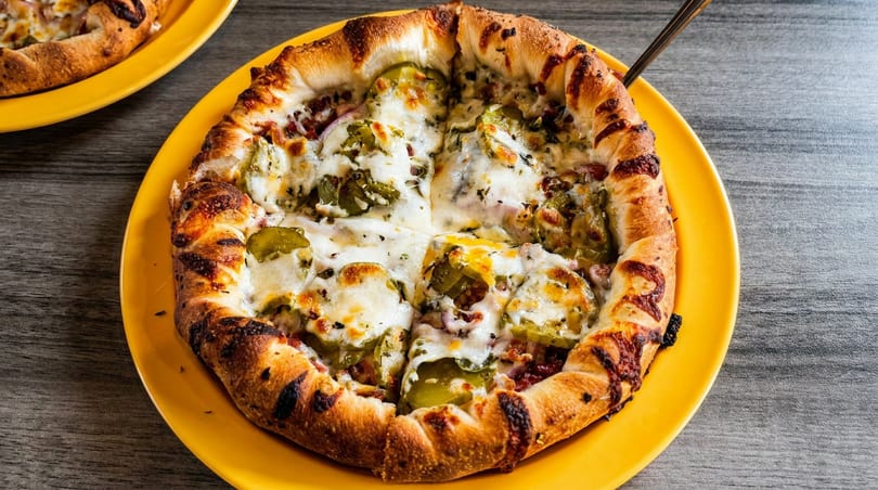 A round, deep-dish pizza with a thick crust, melted cheese, and green peppers on a yellow plate.