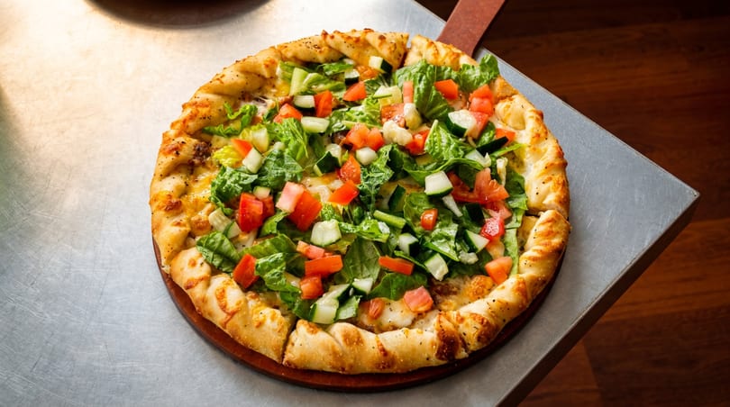 A freshly baked pizza topped with a vibrant salad of lettuce, tomatoes, and cucumbers.