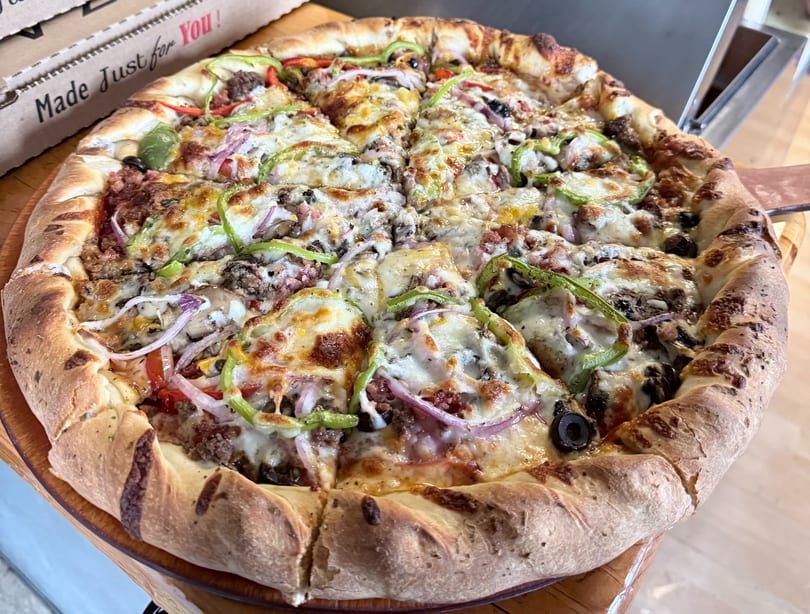 Sliced, thick-crust pizza with melted cheese, green peppers, red onions, olives, and ground meat.